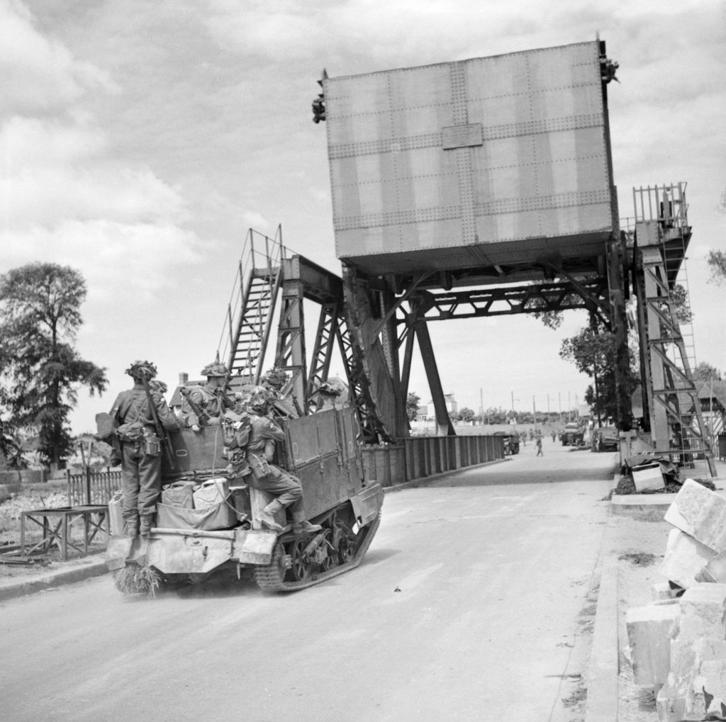A British Universal Carrier crammed with infantrymen heads east across the Caen Canal Bridge following its capture. The canal crossing was renamed Pegasus Bridge as a tribute to the Pegasus insignia worn by British airborne troops who played a vital role in the D-Day invasion. 