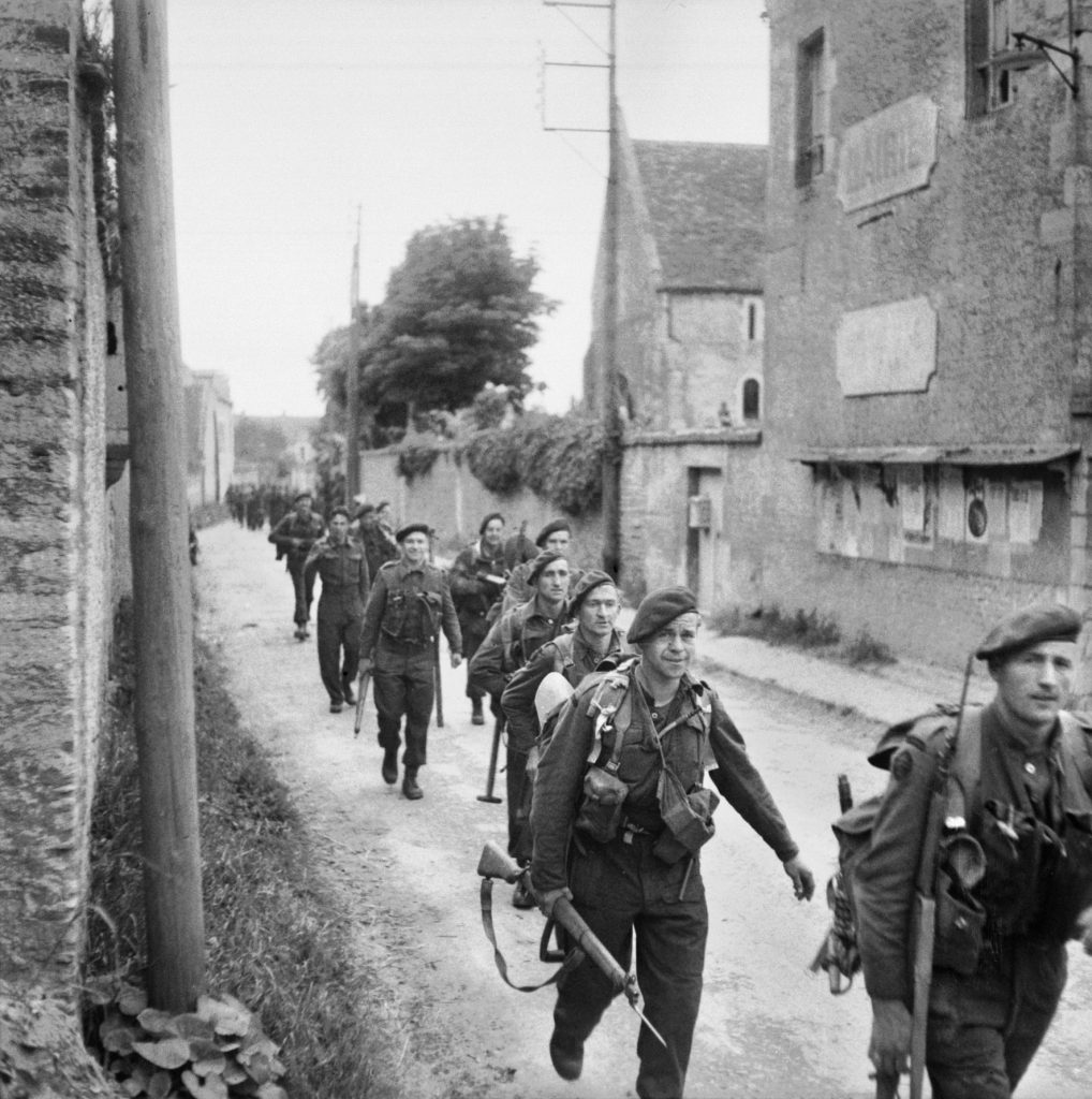 Commandos of the 1st Special Service Brigade, who had just come ashore on Sword Beach, march through Colleville-sur-Orne on their way to relieve the exhausted airborne troops at the two bridges. 