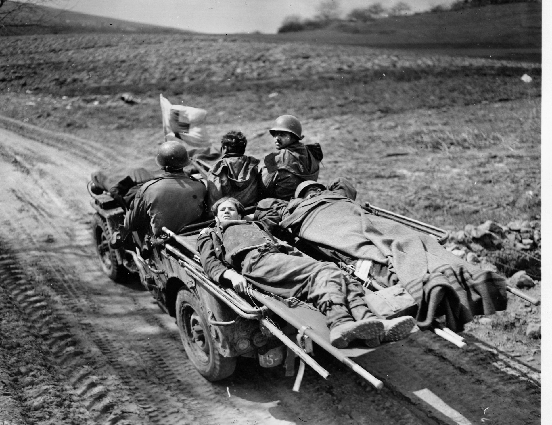Two wounded soldiers, one American and one German, are evacuated from Aschaffenberg in a jeep speeding toward a field hospital. 