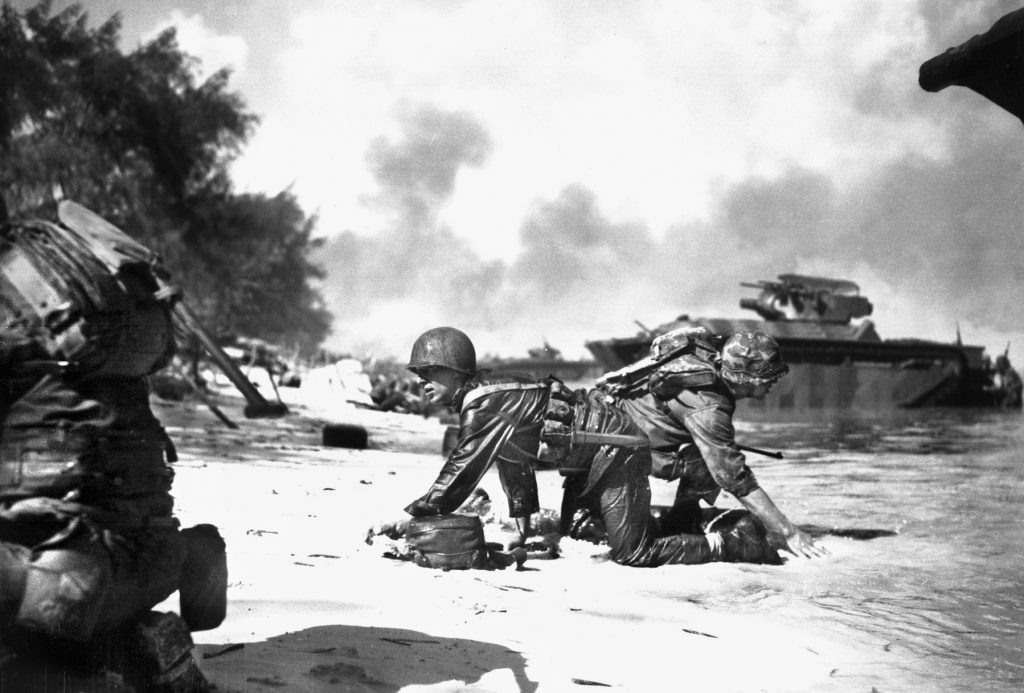 One Marine crawls toward the action on Saipan while another crawls toward his LVT landing craft to retrieve more supplies, June 1943. 
