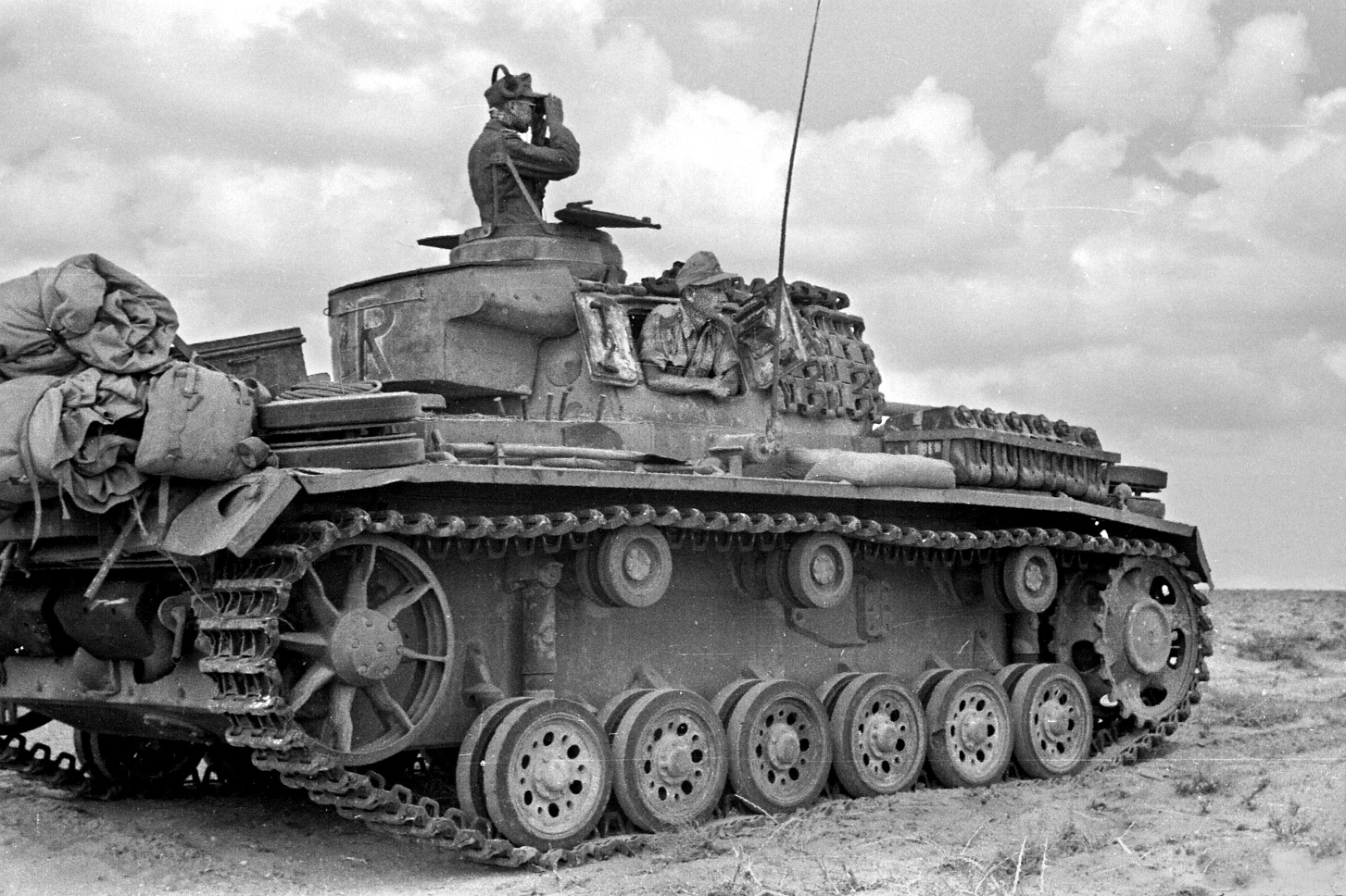 A German tank commander scans the flat, barren desert landscape for any sign of British positions. Fighting in this type of terrain was a challenge for both sides. 