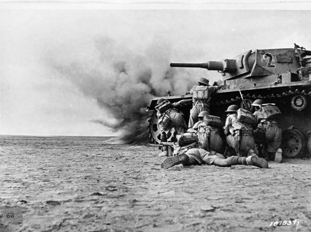 British troops, clad in short pants, take cover behind a knocked-out panzer as they advance toward German lines near El Alamein, where they would win a surprising victory in the autumn of 1942.