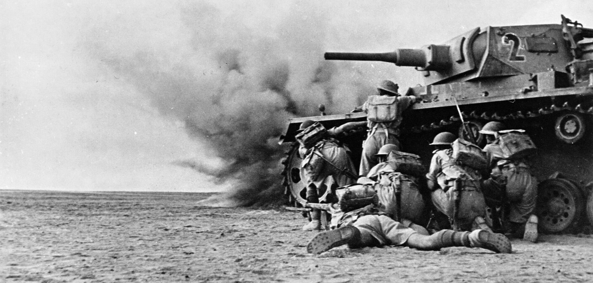 British troops, clad in short pants, take cover behind a knocked-out panzer as they advance toward German lines near El Alamein, where they would win a surprising victory in the autumn of 1942.