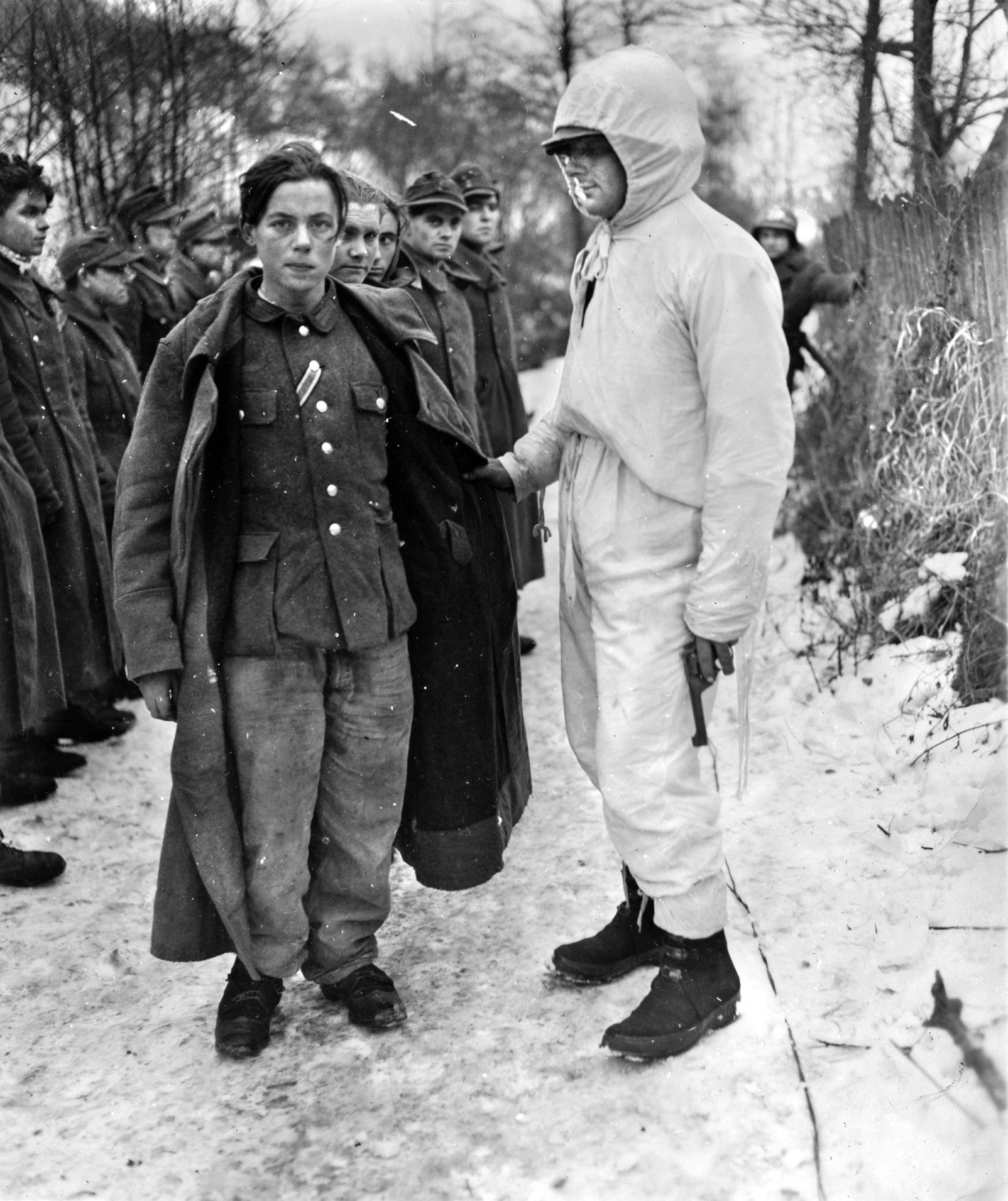 With revolver in hand, an 8th Regiment, 4th Infantry Division, soldier in a snow-camouflage suit takes charge of a group of captured German soldiers near the Sauer River. 