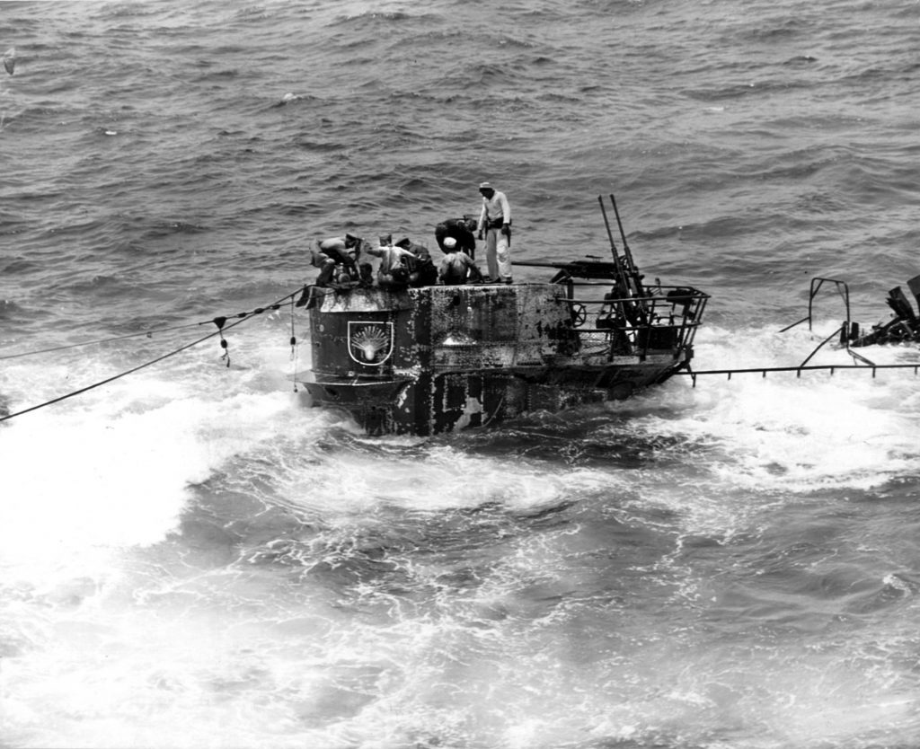 Members of the U.S. Navy boarding party stand in the conning tower of the Type IXC German submarine U-505 while a small pump is used to remove water from the craft and prevent it from being scuttled. The submarine’s twin 20mm antiaircraft gun mount is visible to the rear of the activity.