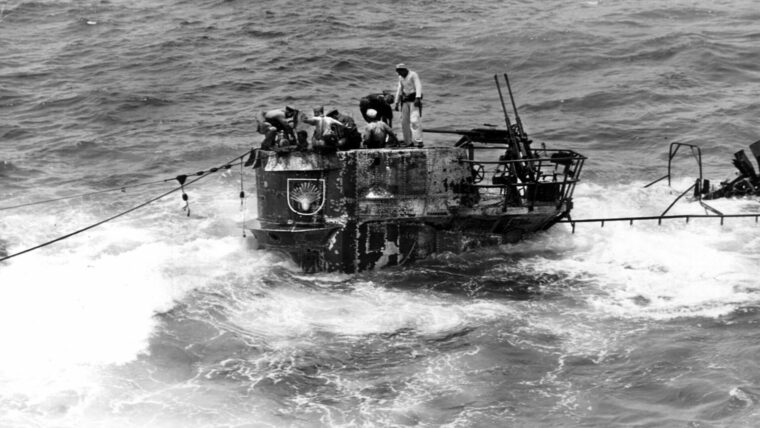 Members of the U.S. Navy boarding party stand in the conning tower of the Type IXC German submarine U-505 while a small pump is used to remove water from the craft and prevent it from being scuttled. The submarine’s twin 20mm antiaircraft gun mount is visible to the rear of the activity.