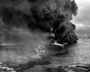 The crew of the battleship USS California abandons ship as smoke billows and burning oil threatens to engulf the stern of the vessel. This photo was taken about 10:00 am, and the capsized hull of the battleship USS Oklahoma is visible at right. California sustained serious damage from bombs and torpedoes and settled to the bottom of the harbor.