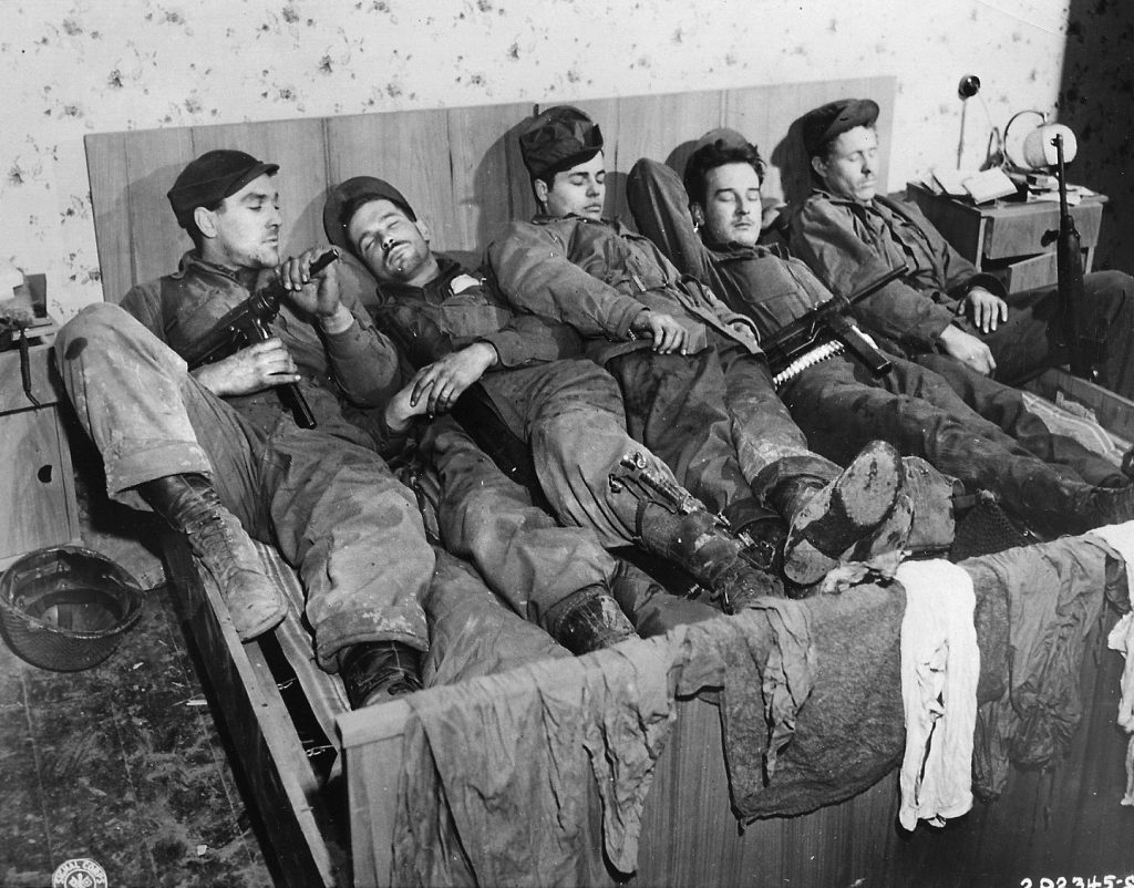Troops of the U.S. First Army grab some sleep during a lull in the fighting near the town of Schmidtheim, Germany. At least two of the soldiers are snoozing with their M3 Grease Guns at the ready, perhaps for the amusement of the photographer.