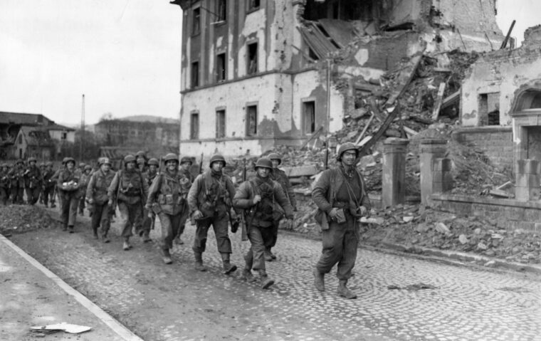 Following six days of fighting to drive German forces from the town of Aschaffenberg, American soldiers march through its ruins.