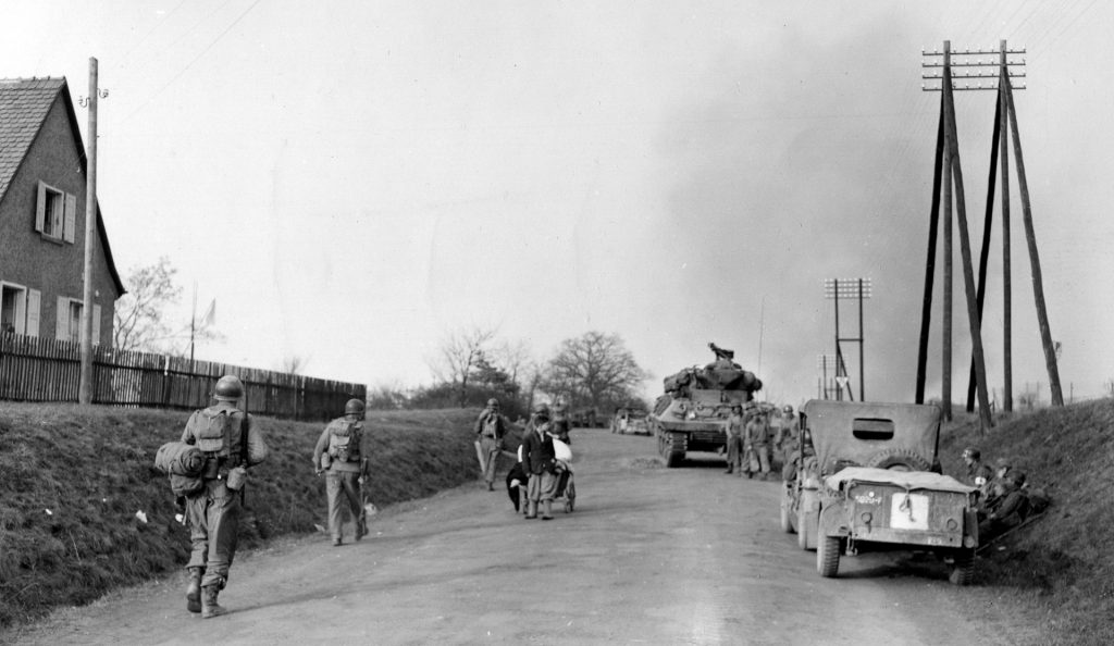 Walking past armored vehicles that have momentarily paused, American soldiers march down the road toward their next objective. The fight for Aschaffenberg was bitter and, in the end, futile for the Germans. 