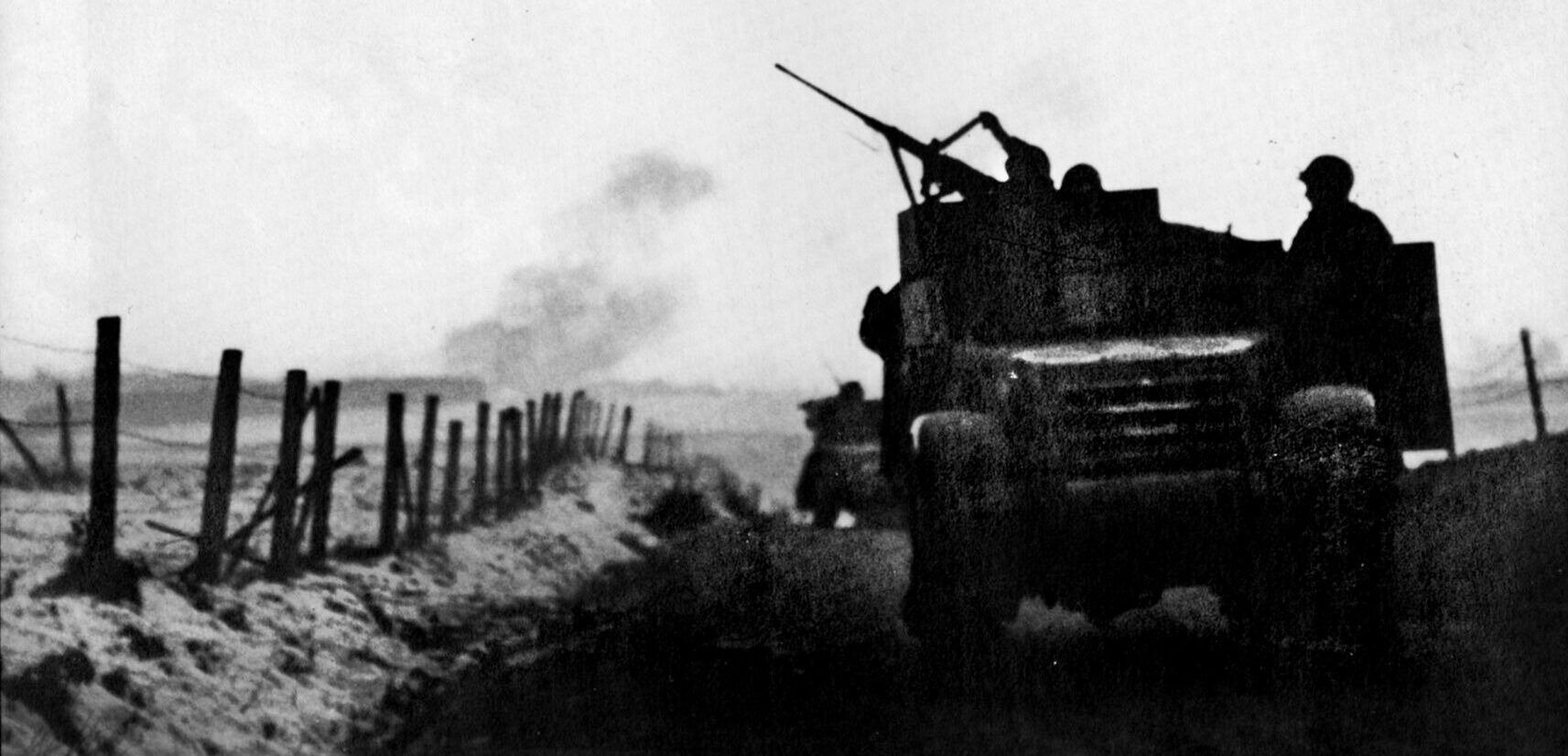 As artillery pounds a German position in the distance, a gunner on a 4th Armored Division halftrack lifts the feed tray cover on his .50-caliber machine gun to reload it. German troops feared the powerful .50 as they had nothing like it. 