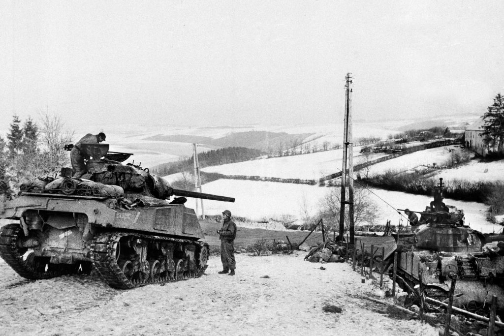 The low hills of the Ardennes region sprawl in the distance as tankers of the 8th Tank Battalion pause near the village of Hotte on December 22. 