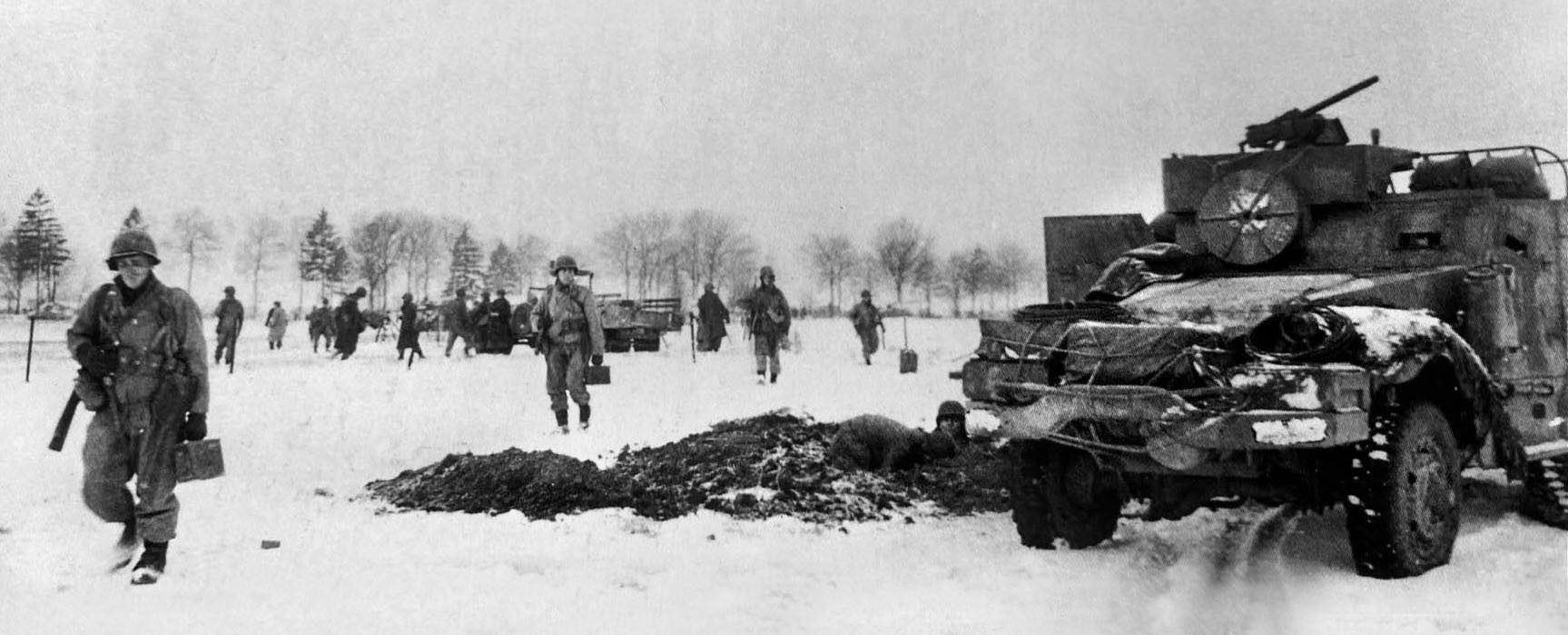 Armored infantry advance near Bastogne. Several GIs are carrying .30-caliber ammunition boxes. The large round object below the half track’s machine gun is a spool for communications wire. 