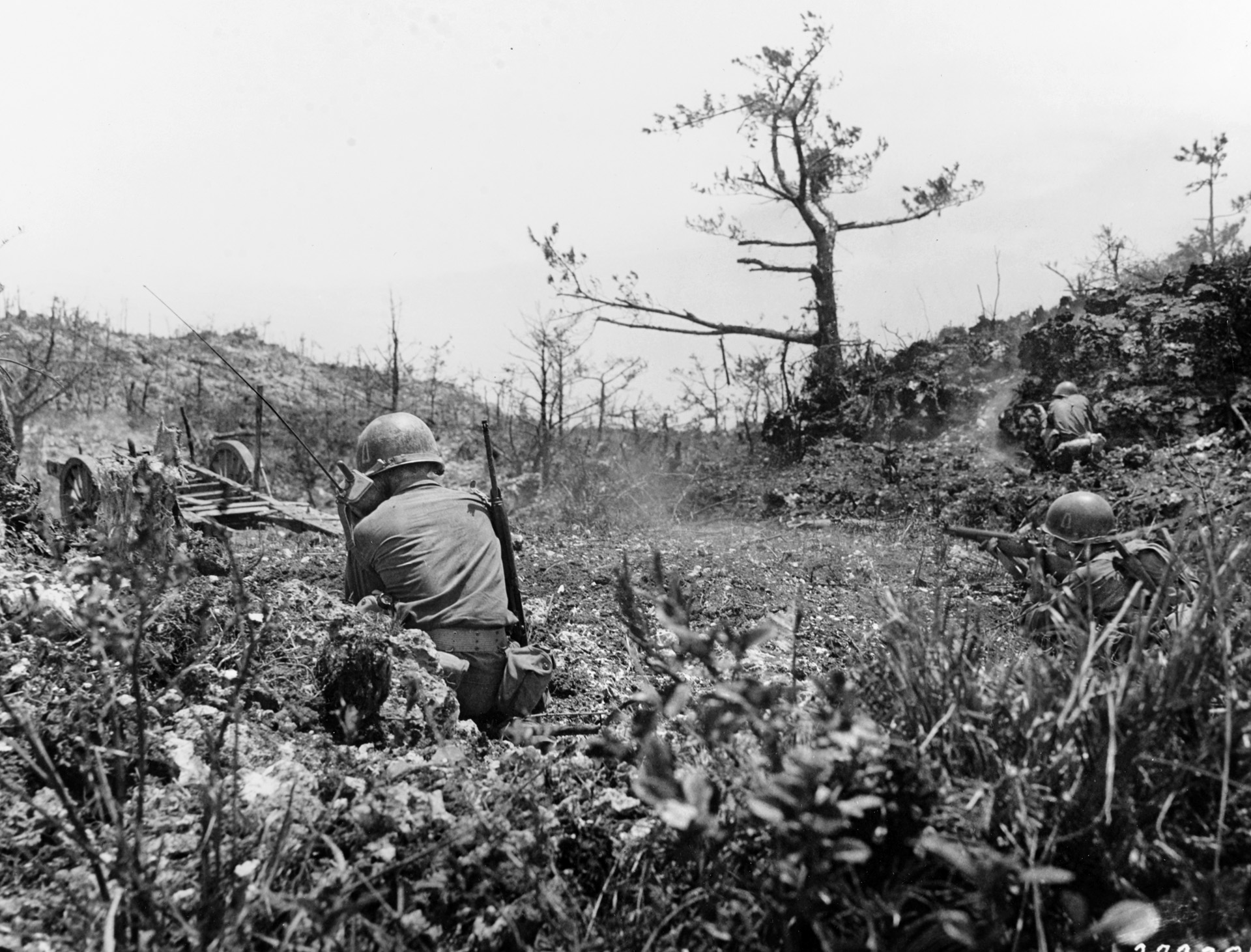 An American radio operator relays the progress of an attack against well entrenched Japanese troops on Okinawa as infantrymen from the Army’s 77th Division fire on a fortified position carved into an escarpment.