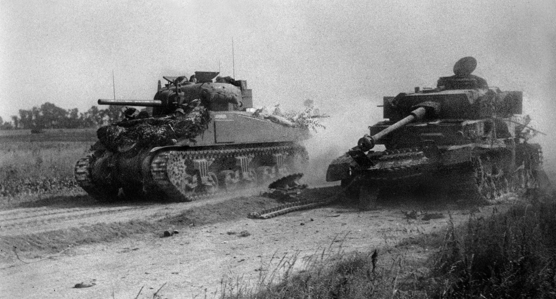 A British M4 Sherman medium tank races past a knocked-out German PzKpfw. IV tank during the desperate fight for control of the crossroads and communications hub of Caen during the weeks after D-Day. Allied planners had projected that Caen would be in British hands on D-Day itself; however, a month of bitter fighting was required for Allied forces to capture the town.