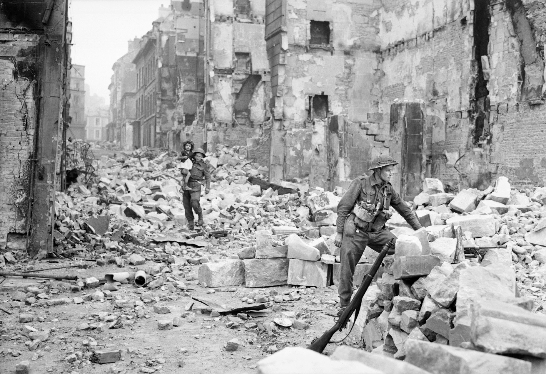 British troops patrol Caen. Royal Air Force medium and heavy bombers pulverized the city during two separate bombing raids, killing many civilians but causing few German casualties. 