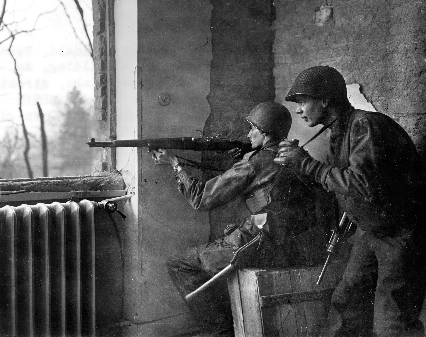 Two soldiers of the 90th Division exchange fire with German troops from a second-story window. The 358th Infantry Regiment stopped the German Armored column in Mairy and captured more than 200 German prisoners.