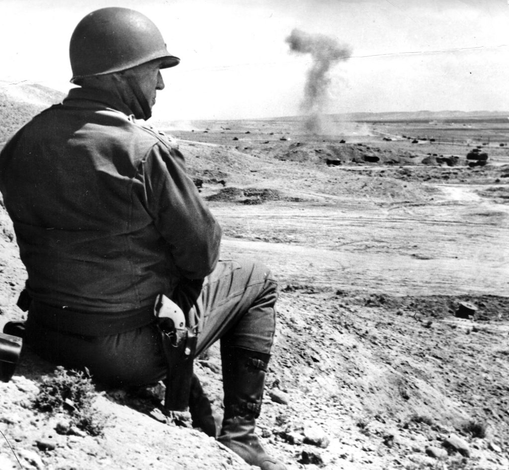 Lieutenant General George S. Patton watches American tanks from his II Corps advance against Axis forces in Tunisia. He had taken command of the corps, defeated at Kasserine Pass, twelve days earlier and sent it into battle. 