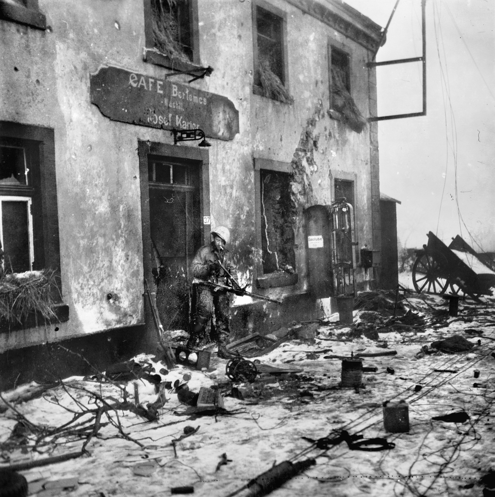 An American soldier, the whitewash camouflage on his helmet faded, inspects a captured German MG 42 in the ruins of a Luxembourg village. 
