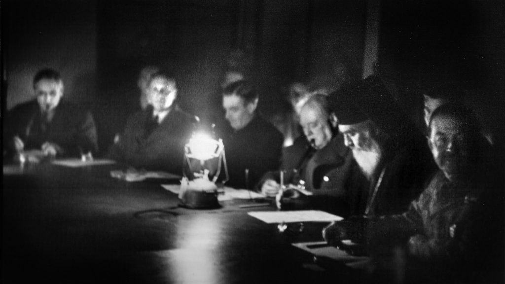 British Prime Minister Winston Churchill (center right) engages in negotiations with Archbishop Damaskinos Papadreou in December 1944. The talks are being conducted by candlelight due to a power outage that resulted from the heavy fighting in Athens.