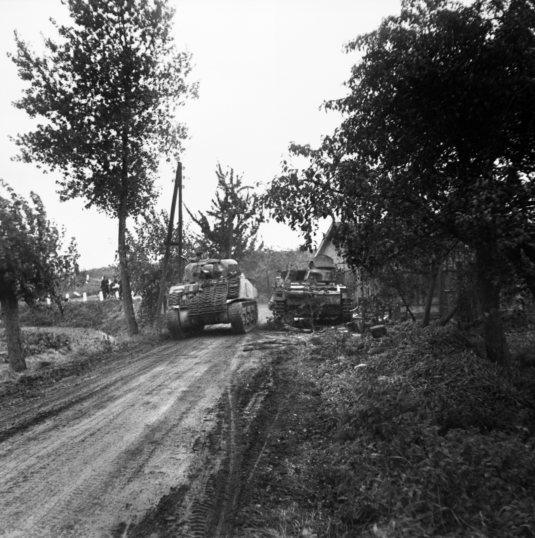 A British M4 Sherman medium tank of the 47th/7th Dragoon Guards passes the wreckage of a German PzKpfw. III tank along a dirt road on the edge of the Dutch village of Oosterhout. 