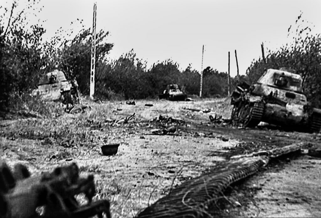 This still photo taken from documentary film footage shot several days after the fighting for the La Fiere bridge ended is mute testimony to the ferocity of the contest. Three French-built tanks, deployed by the Germans during a counterattack, sit knocked out and abandoned. A concrete telephone pole similar to those shown in this image provided cover for the paratroopers firing bazookas at the oncoming tanks until it was toppled by a round from one of the armored vehicles.