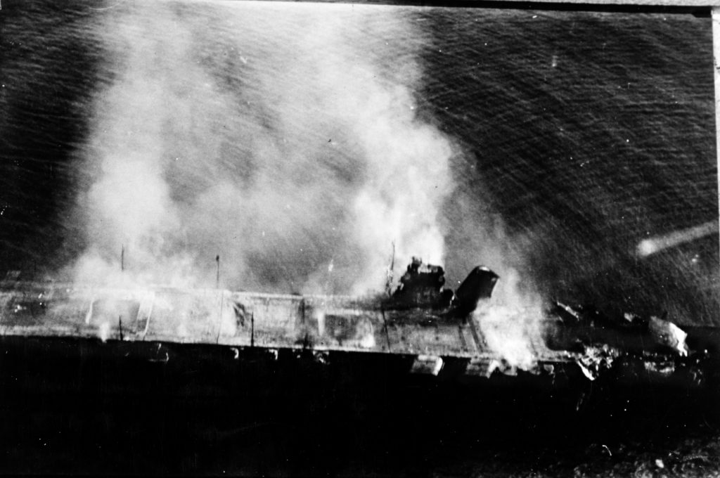 Smoke billows from the stricken aircraft carrier Hiryu shortly after sunrise on June 5, 1942. Hiryu had been heavily damaged during a raid by American dive bombers the previous day, and a portion of the carrier’s forward elevator stands upright just forward of the island, where it had been blown after a tremendous explosion on the hangar deck below.