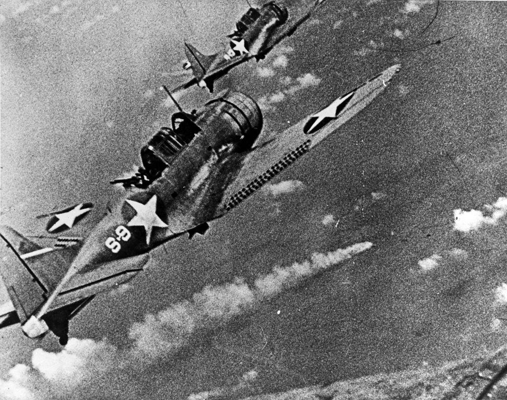 This enlarged frame from a color 16mm motion picture film became one of the most famous photographs of World War II in the Pacific. It depicts two Douglas SBD Dauntless dive bombers from the aircraft carrier USS Hornet bearing down on the stricken Japanese heavy cruiser Mikuma on the afternoon of June 6, 1942. Mikuma, already seriously damaged during earlier raids by dive bombers from the carriers Hornet and USS Enterprise, sank later in the day.