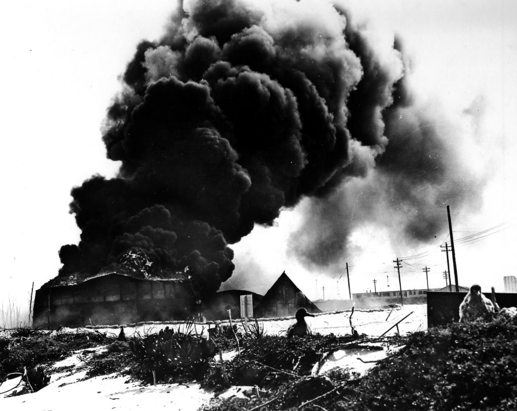 Oil tanks on Sand Island, one of two spits of land that make up Midway Atoll, burn furiously on the morning of June 4, 1942, following an attack by Japanese carrier-based aircraft. A pair of albatrosses, nicknamed gooney birds, for which the atoll was well known prior to the battle, are seen in the foreground.
