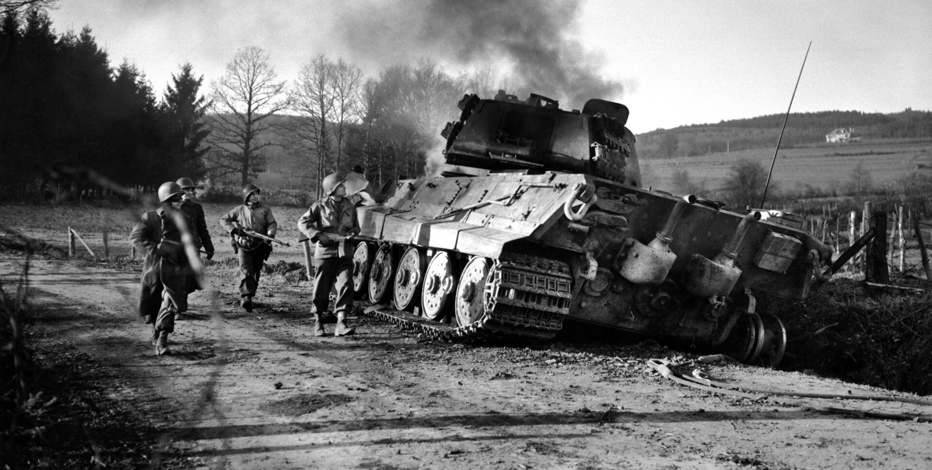 American soldiers inspect a German tank that has been knocked out during the Battle of the Bulge. Despite initial successes, the German advance was stymied as pockets of defenders made heroic stands against the enemy, disrupting the precise German timetable. The initial Intelligence failure, however, cost the Americans dearly in terms of casualties and equipment lost.