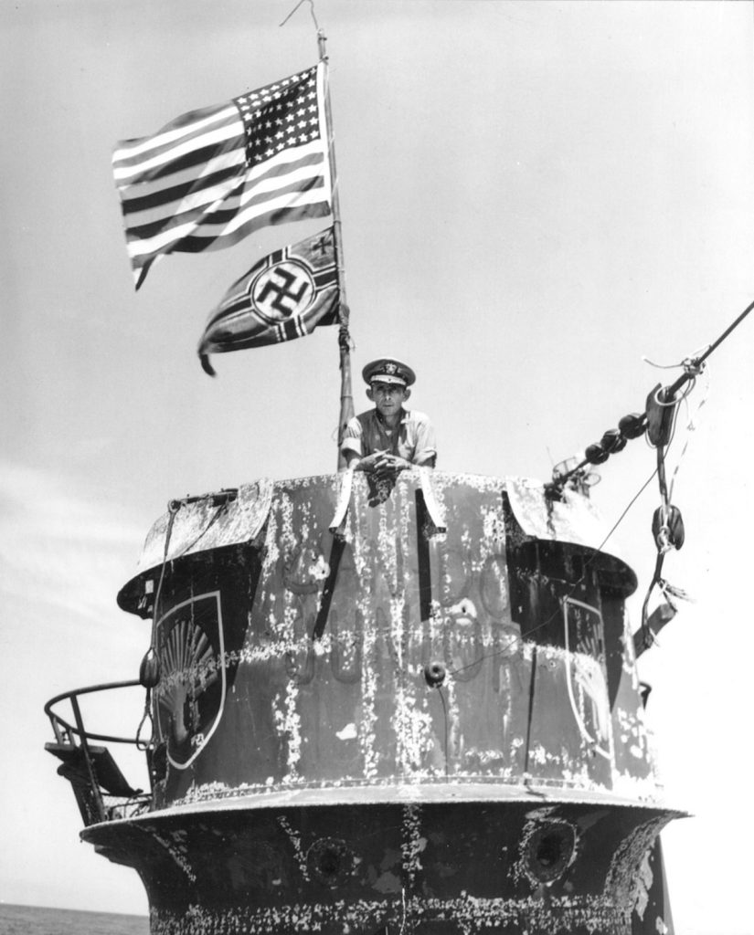 Captain Daniel V. Gallery, Jr., commander of the escort carrier USS Guadalcanal, poses on the conning tower of U-505 prior to the U-boat’s being taken in tow for the voyage to Bermuda. The German submarine’s crest, an embellished scallop shell, is visible on both sides of the conning tower.