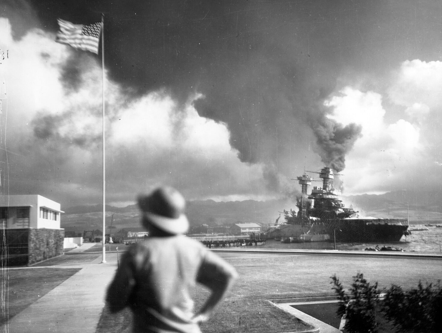  A survivor appears to look for Japanese aircraft beyond the defiant American flag on Ford Island as California lists to port after taking bomb and torpedo hits from marauding Japanese aircraft. 