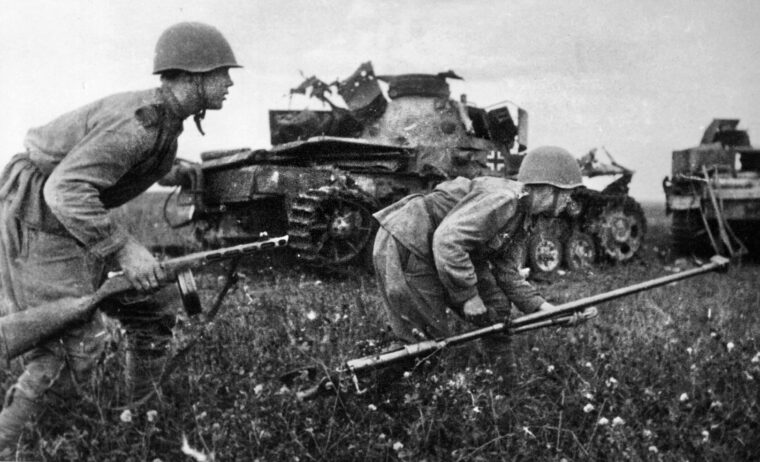 Soviet infantrymen crouch as they rush past the mangled wreckage of German tanks. The soldier at right carries a heavy antitank rifle, which was woefully ineffective against German medium and heavy tanks.
