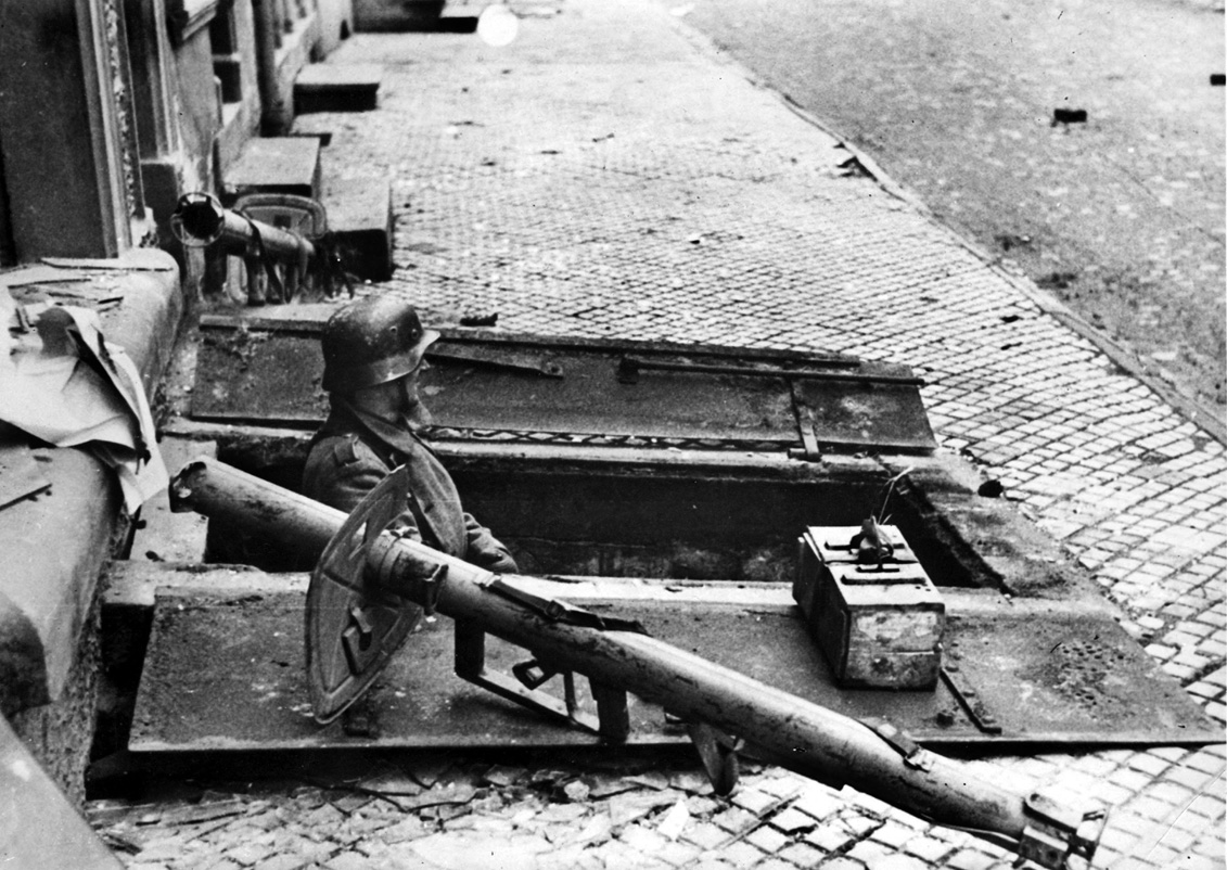A German soldier armed with a Panzerschreck antitank rocket launcher, peers from a cellar.