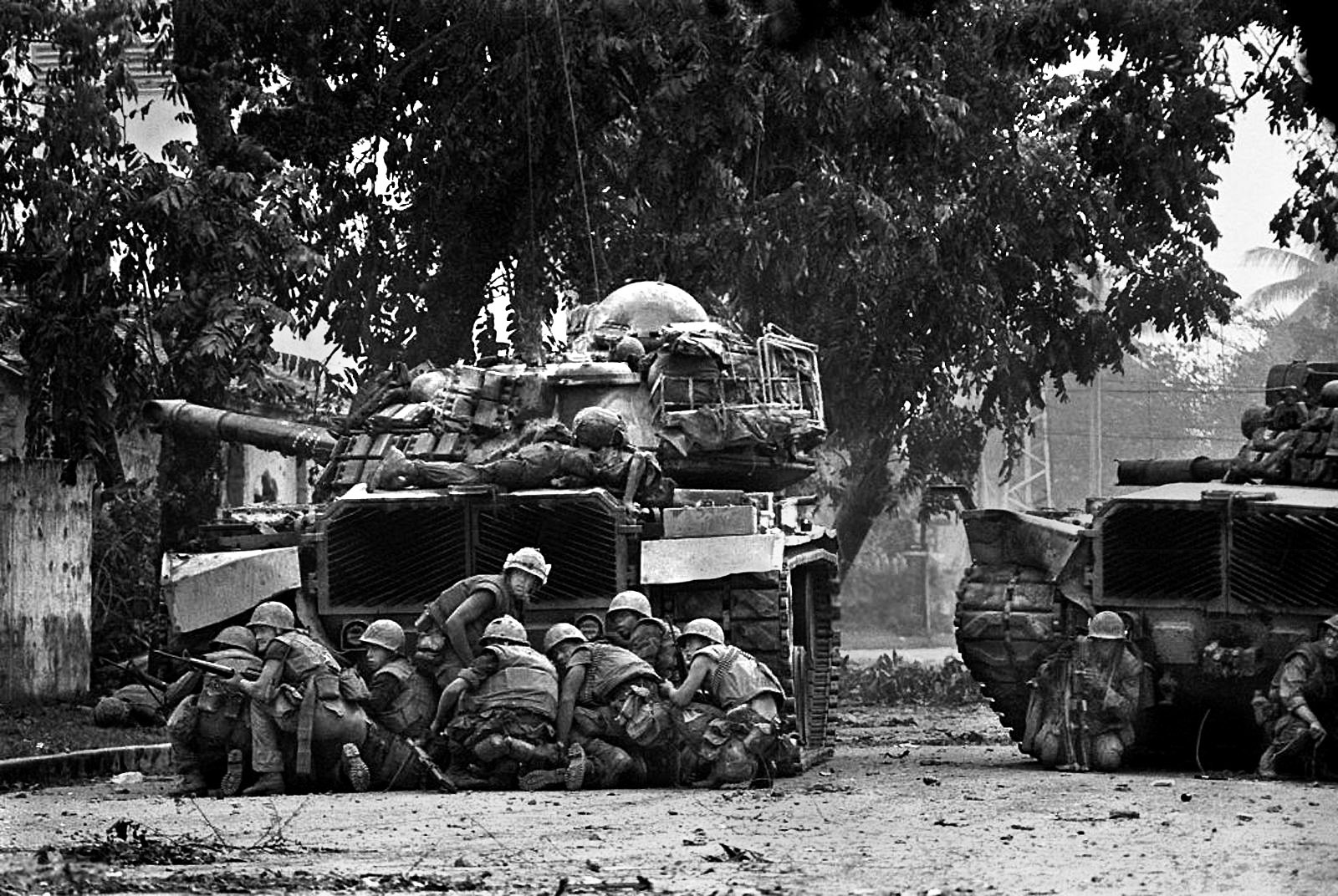 A Patton tank fires on a North Vietnamese position as Marines take cover from an enemy sniper. 
