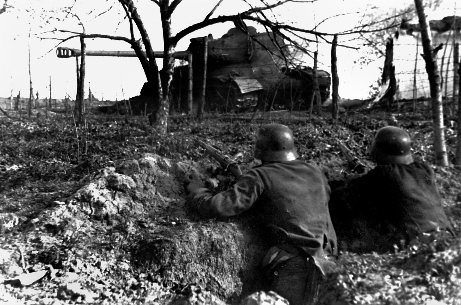 Entrenched German soldiers armed with K98 rifles hold a position behind a wrecked tank. The Germans had constructed three fortified lines with mines and obstacles to blunt the Soviet attack against Berlin. 