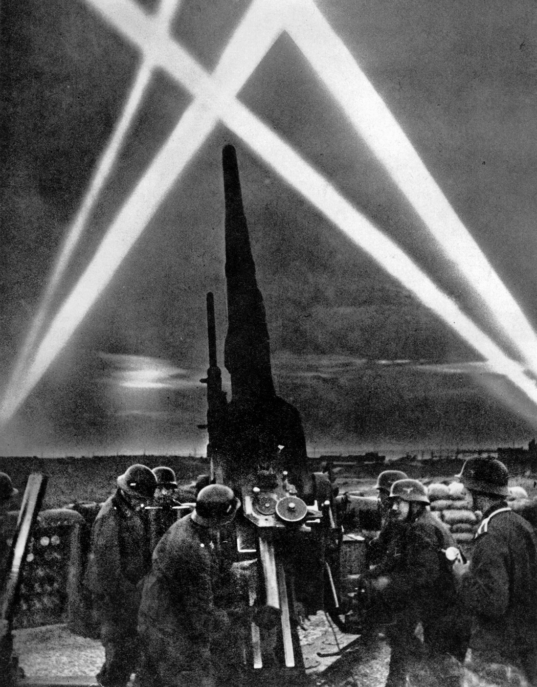 A German antiaircraft gun crew prepares for action in 1940, as searchlights pierce the night sky to illuminate targets for the gunners.  