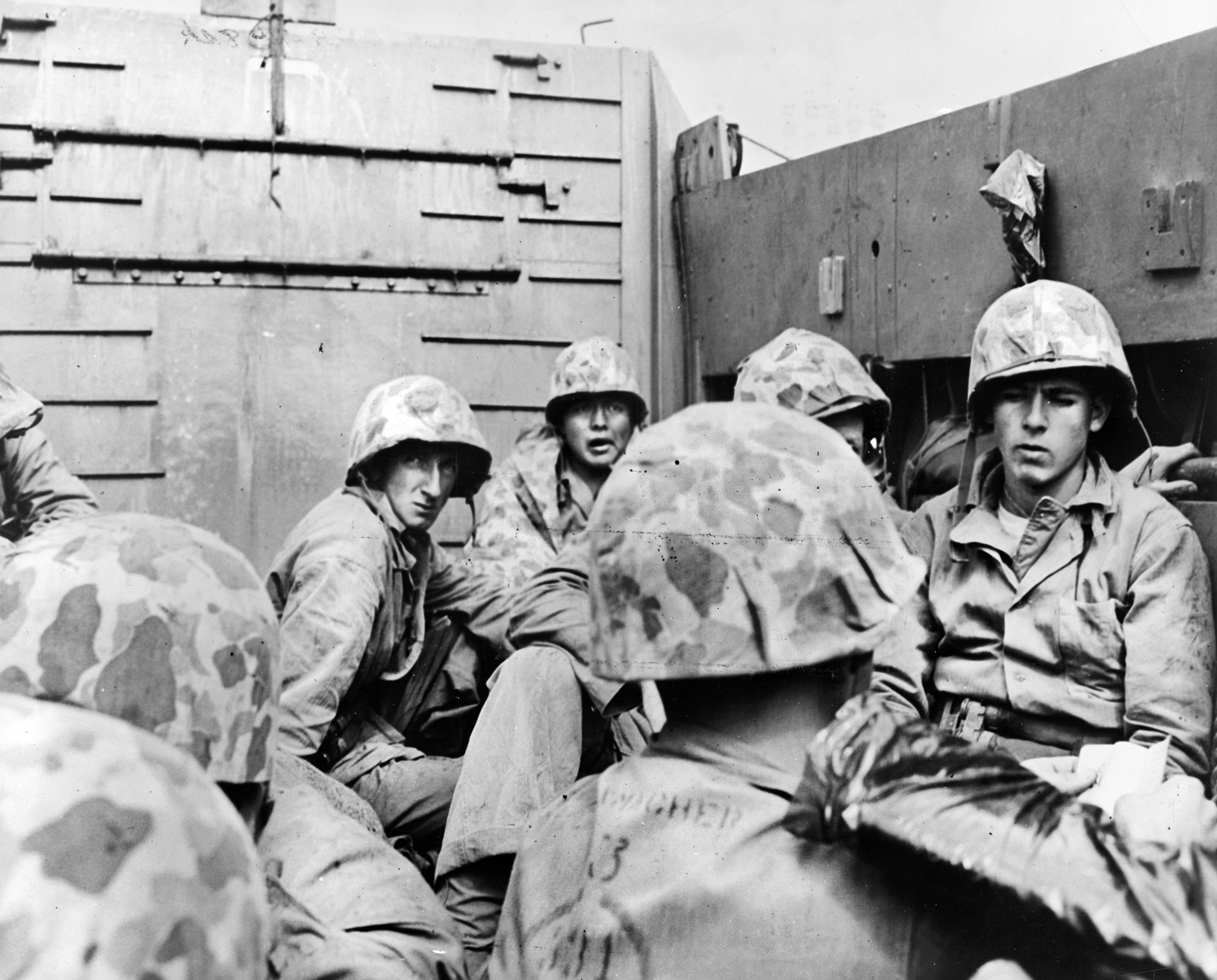 Grim-faced Marines in camouflaged helmets stay low as they head toward the beach in a Coast Guard-manned landing craft. 