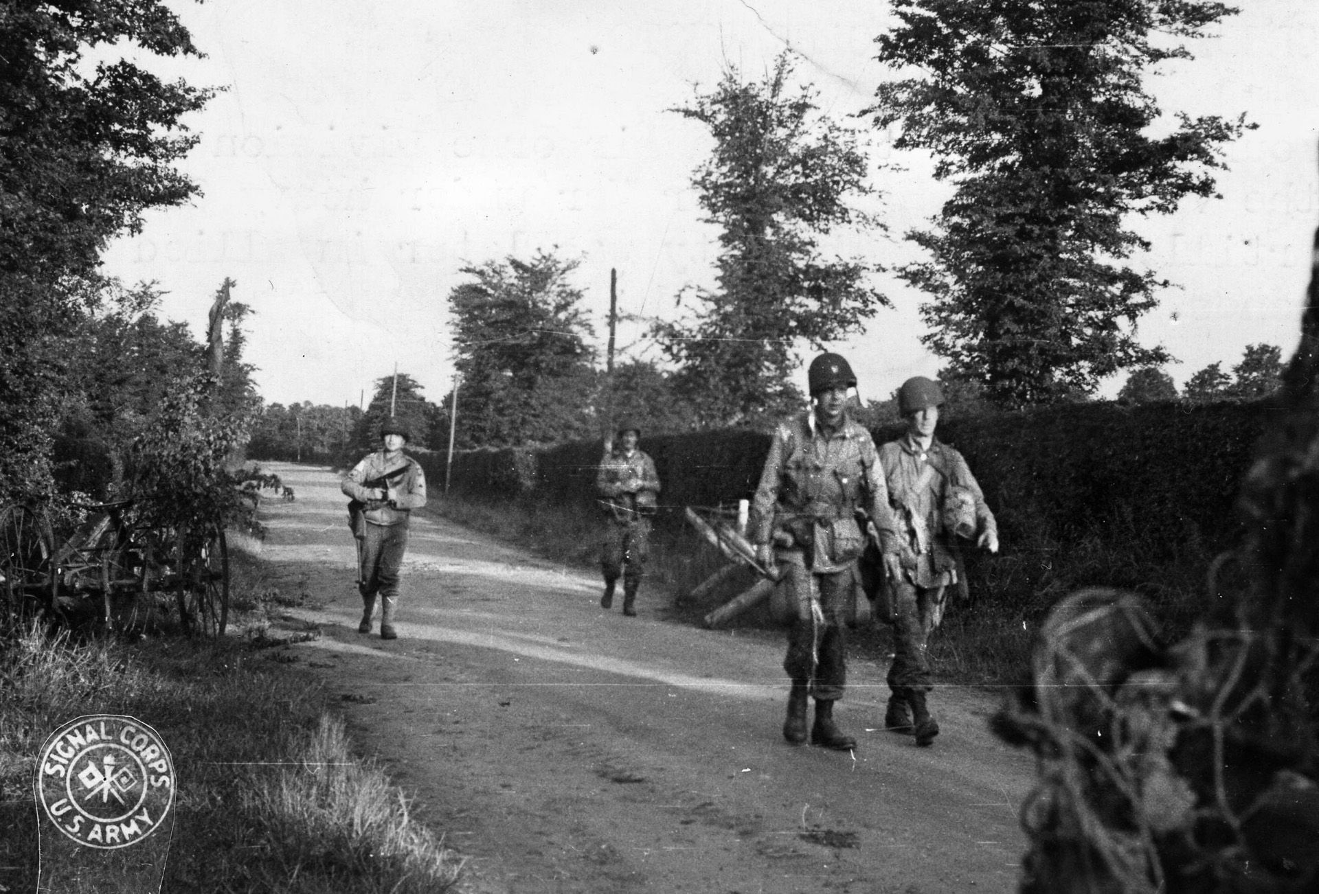 Near the village of Ste. Mere Eglise, which they captured on D-Day, paratroopers of the 82nd Airborne Division walk along a road lined with hedgerows. 