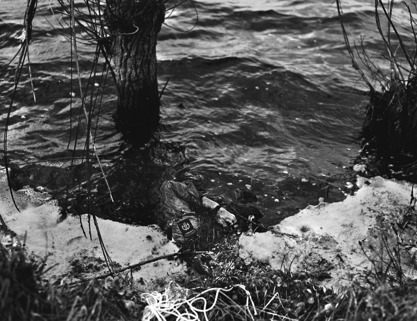 The body of a drowned 82nd Airborne paratrooper, weighed down by the load of his parachute pack and equipment, floats quietly in a flooded field somewhere in Normandy. The Germans intentionally flooded the area to make airborne landings and cross-country movement difficult for the invaders.