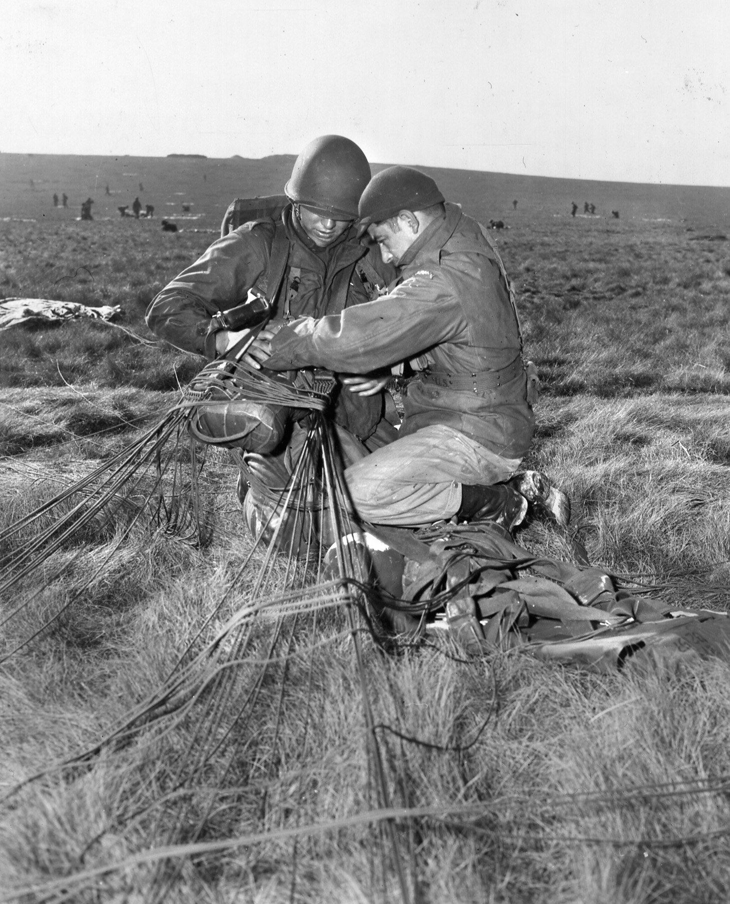 After coming to earth, a paratrooper of the 82nd Airborne Division helps his comrade disengage from the tangled lines of his parachute.
