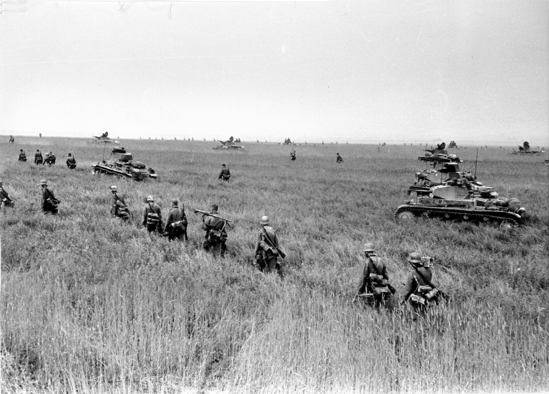 German infantry and Panzers move across open fields in France, following their breakthrough in the Ardennes.