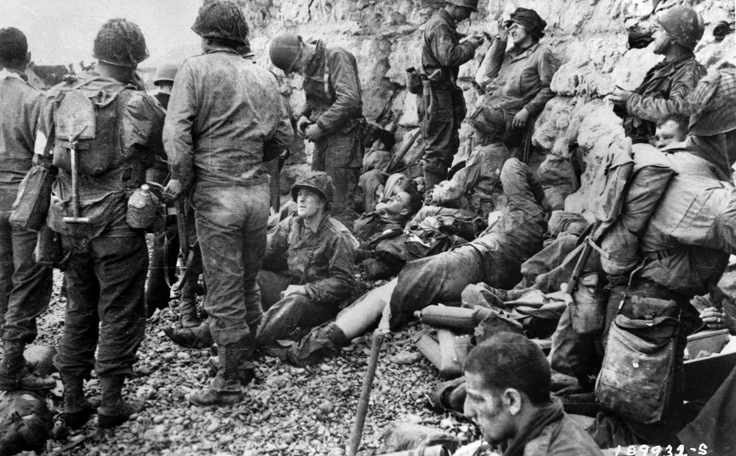 Having just survived the hellish boat ride into shore, a group of wounded 1st Division soldiers take shelter along a cliff face at Colleville-sur-Mer to await evacuation to a hospital ship. 