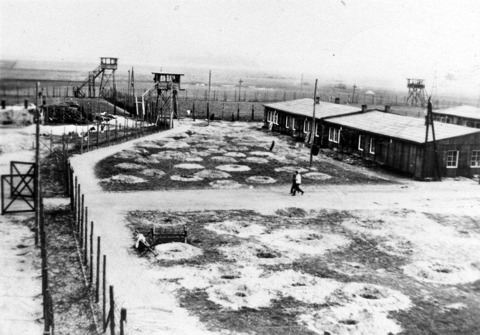Three empty guard towers are shown along the barbed-wire enclosure of Stalag Luft 1 after the guards abandoned the camp. The many circular holes are for personal protection in the event of an air raid. 