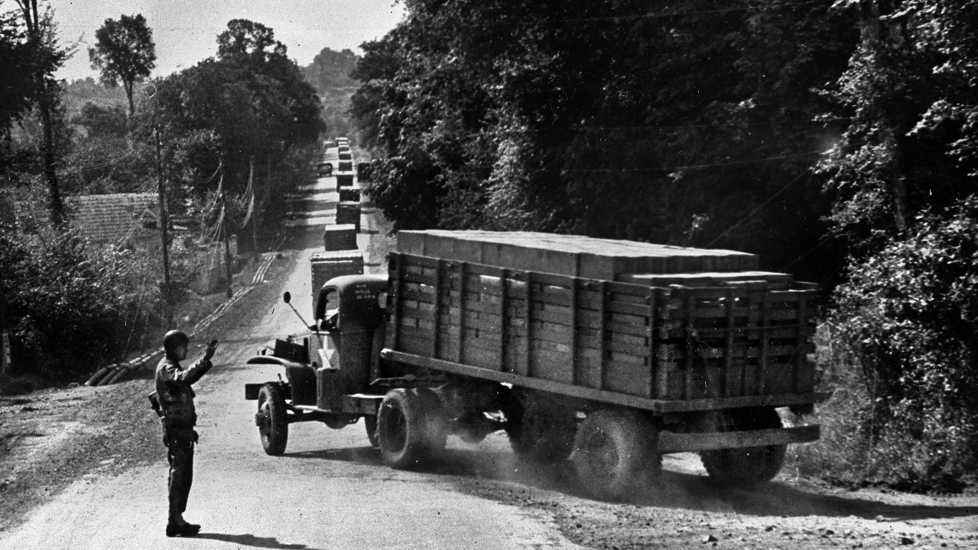 The road to victory: A military policeman waves through another truck rushing cargo on a one-way highway to the fast-moving front lines in Normandy, France, August 1944. The mostly African American drivers of the Red Ball Express realized that without a steady stream of food, fuel, ammunition, medical equipment, troops, and other critical supplies, the Allied advance would grind to a halt.
