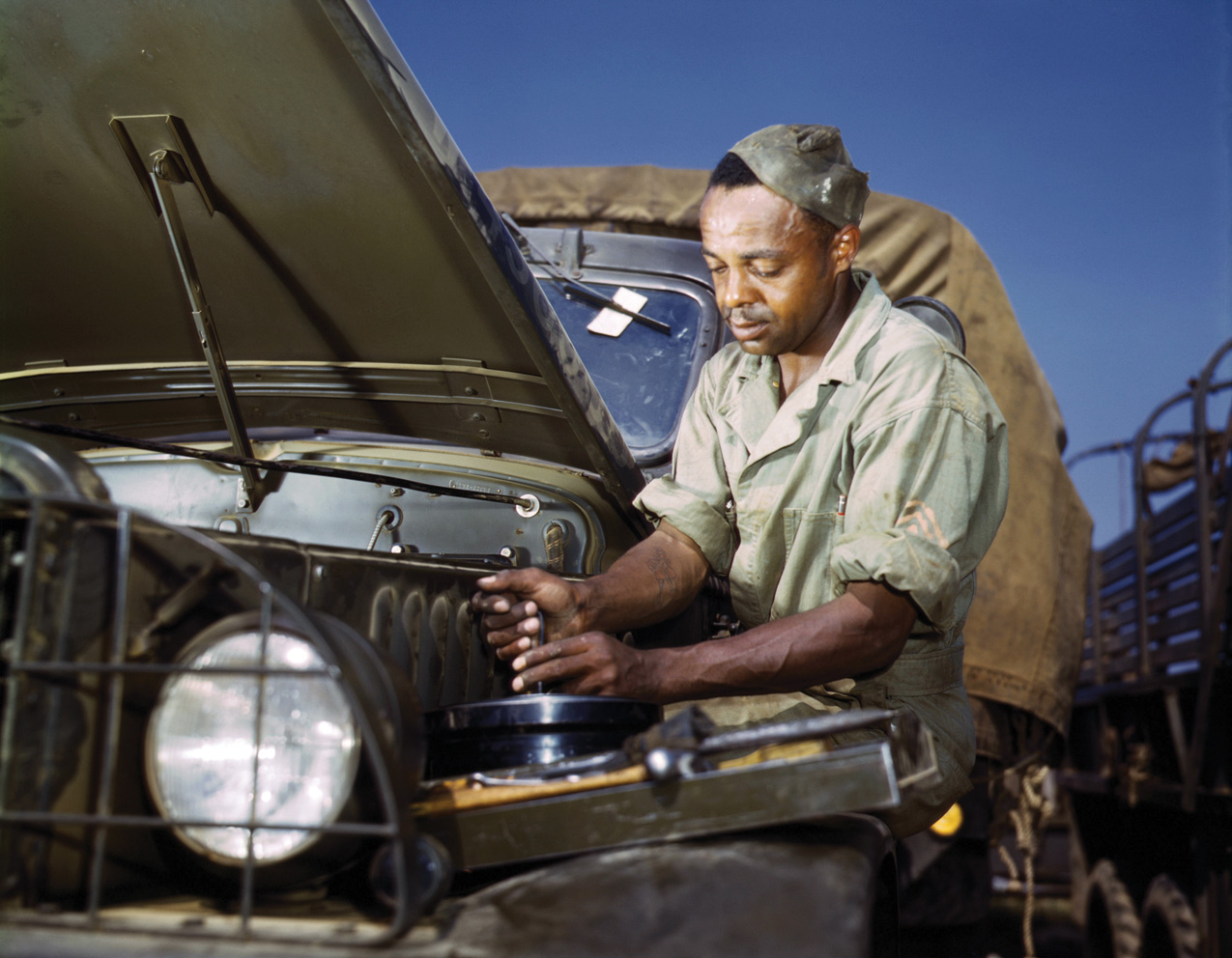 A Black soldier, who is both driver and mechanic, performs maintenance in the field. The constant hard usage quickly wore out the trucks.