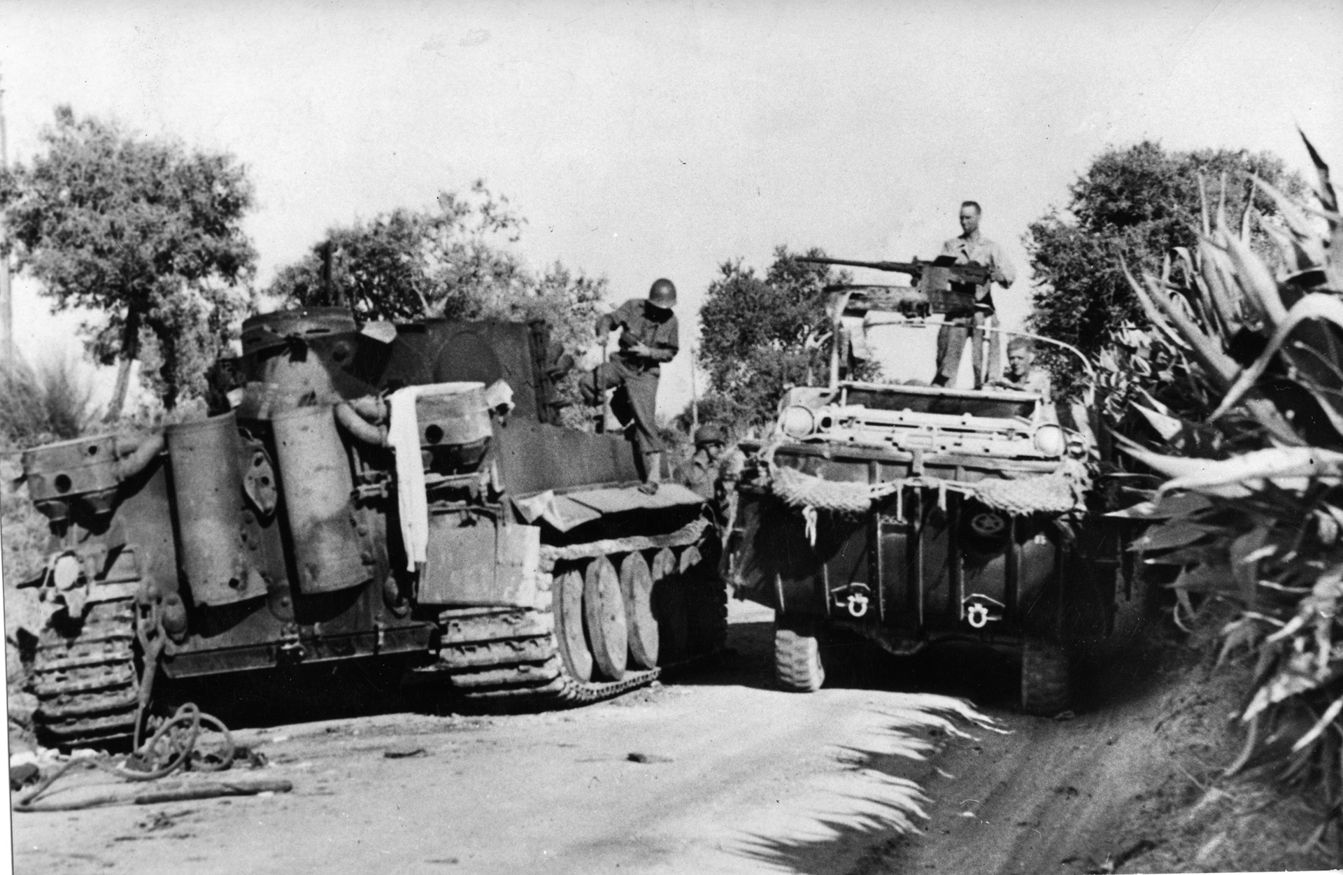 An American DUKW (amphibious vehicle) squeezes past a disabled German Tiger tank that blocks the road to Sicily’s northern coast.