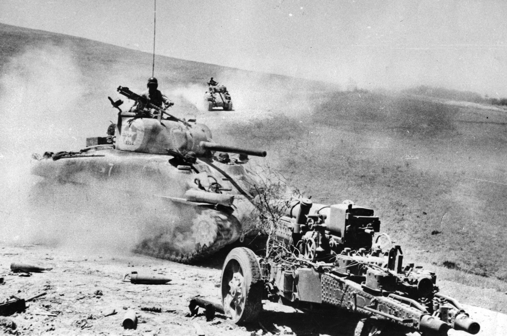 Sherman tanks raise dust on their way to Palermo, rolling past an abandoned Italian 149/19 field piece. The Italians had little stomach for the fight, leaving much of the defense of Sicily to the Germans.