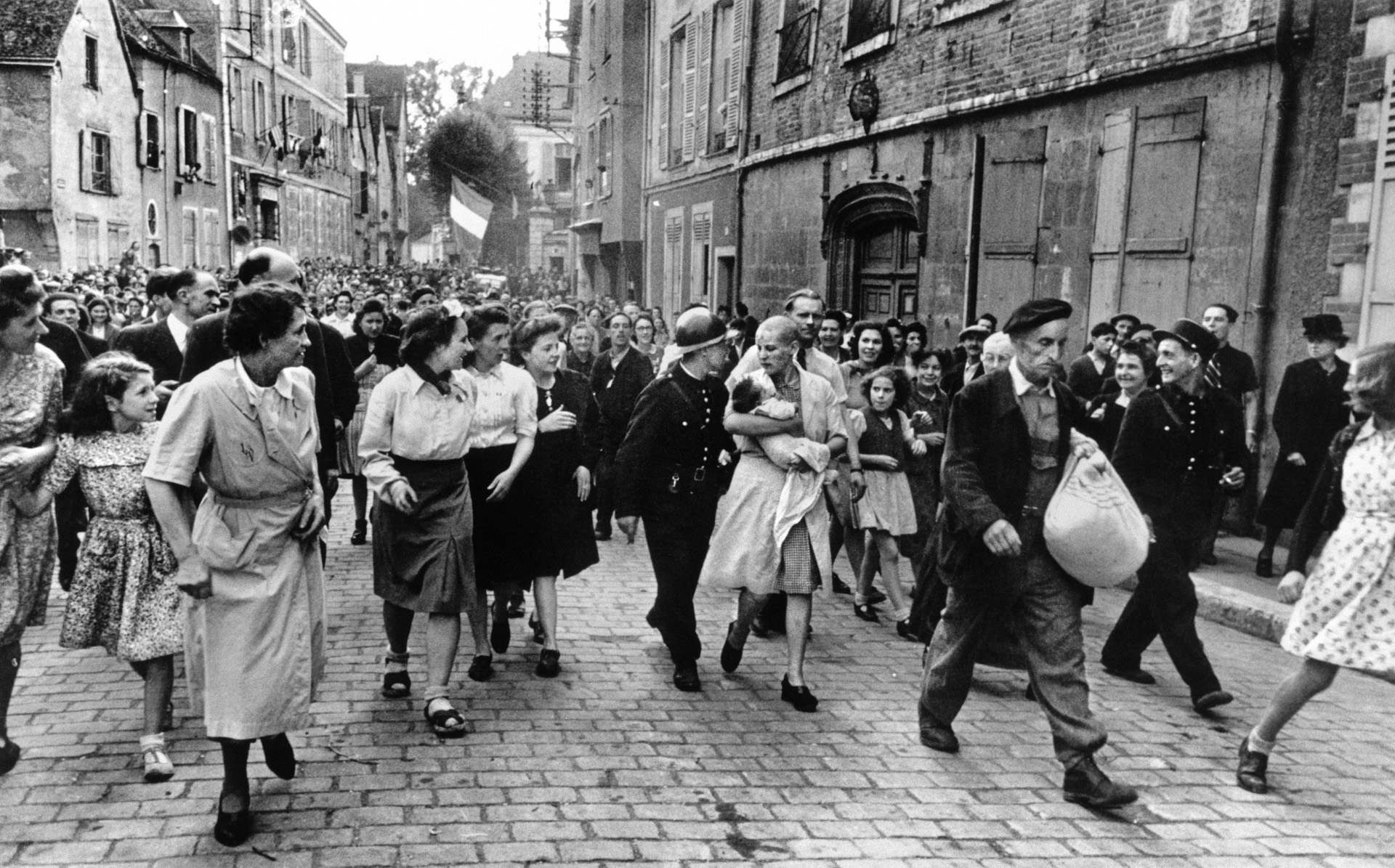 The French were brutal to their countrymen who collaborated with the Germans. Here a woman, whose head has been shaved, carries her baby by a German soldier through a crowd of angry civilians in Chartres.