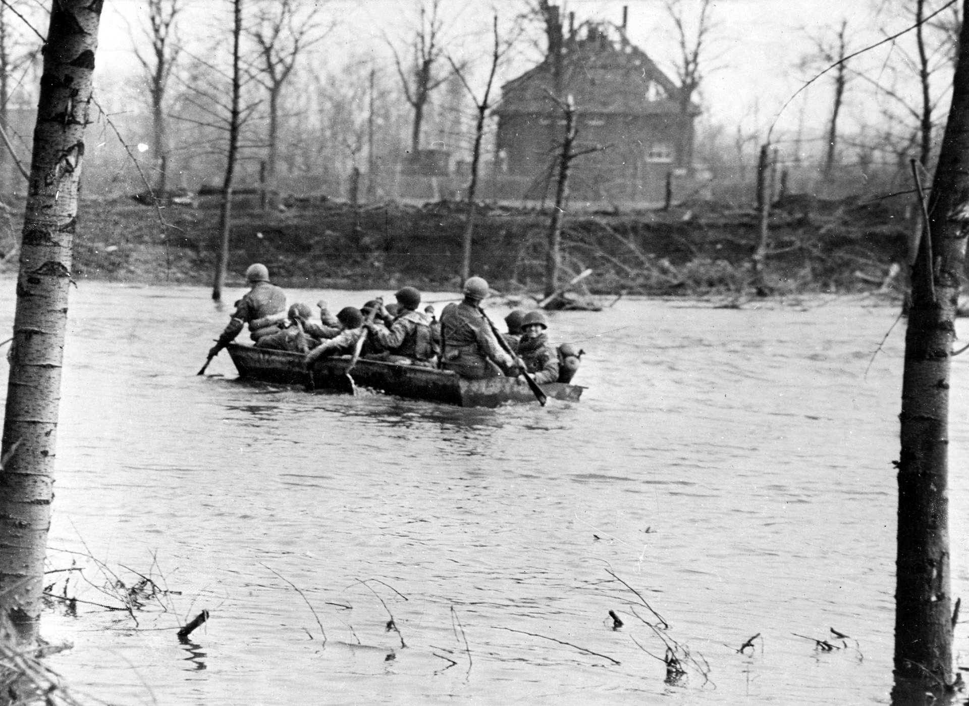 With most of the bridges destroyed by the retreating enemy, Ninth Army troops in assault boats paddle their way across the fast-flowing Roer River near Goch, in the Reichswald. 
